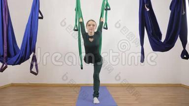 年轻的白种人妇女在室内工作室的吊床上做反重力飞行瑜伽练习。 航空飞行健身